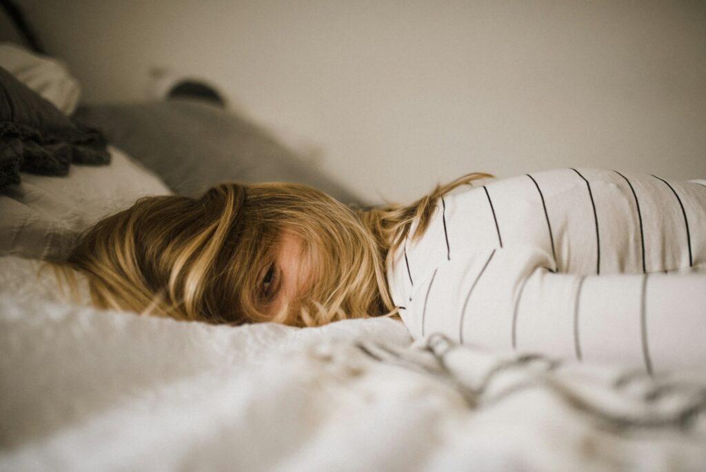 Moe vrouw met haren over gezicht op bed, symbool voor stress en oververmoeidheid