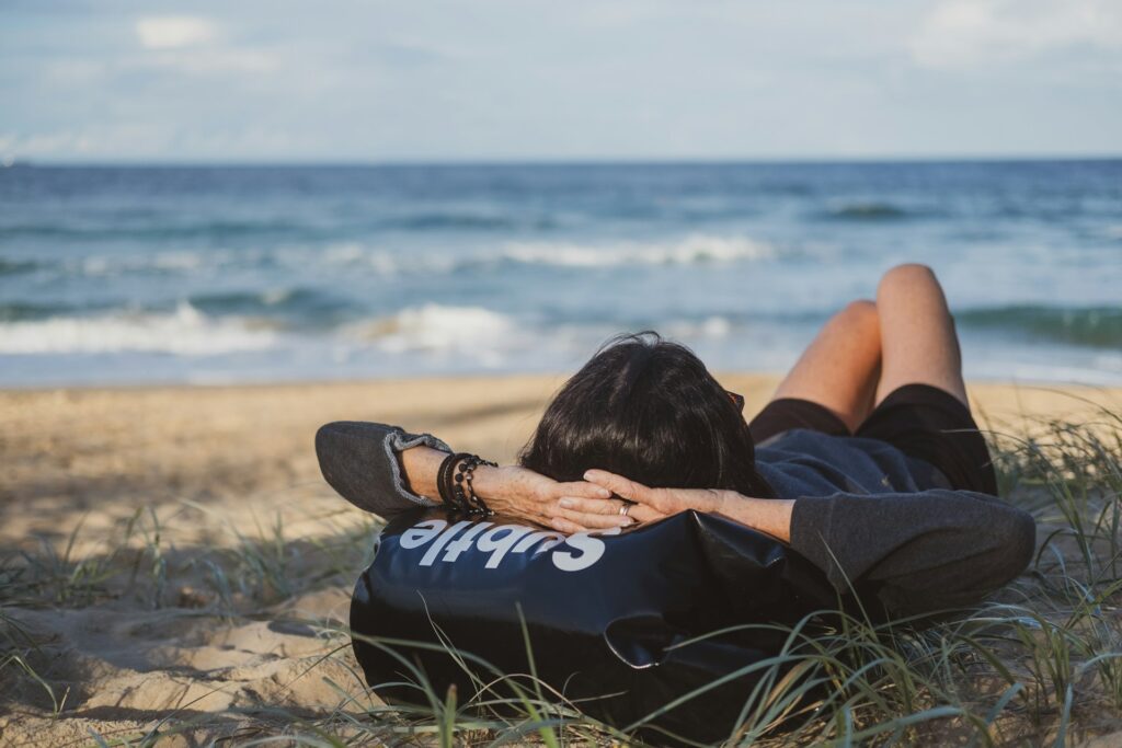 Ontspannen vrouw ligt op een strand en kijkt uit over de zee, symbool voor het loslaten van schuldgevoel